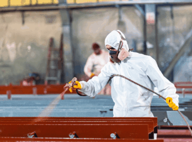 Trabalhador usando EPI aplicando pintura industrial com pistola em estrutura metálica