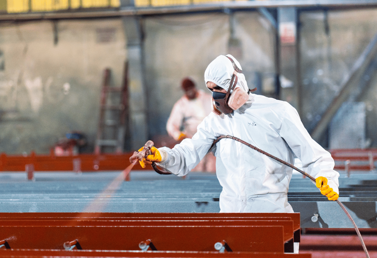 Trabalhador usando EPI aplicando pintura industrial com pistola em estrutura metálica