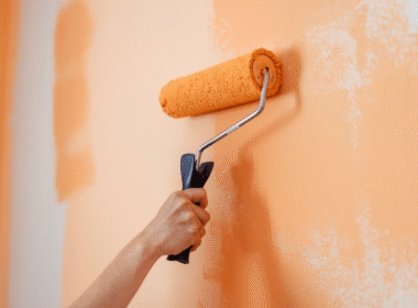 Pessoa aplicando tinta laranja na parede com rolo de pintura.